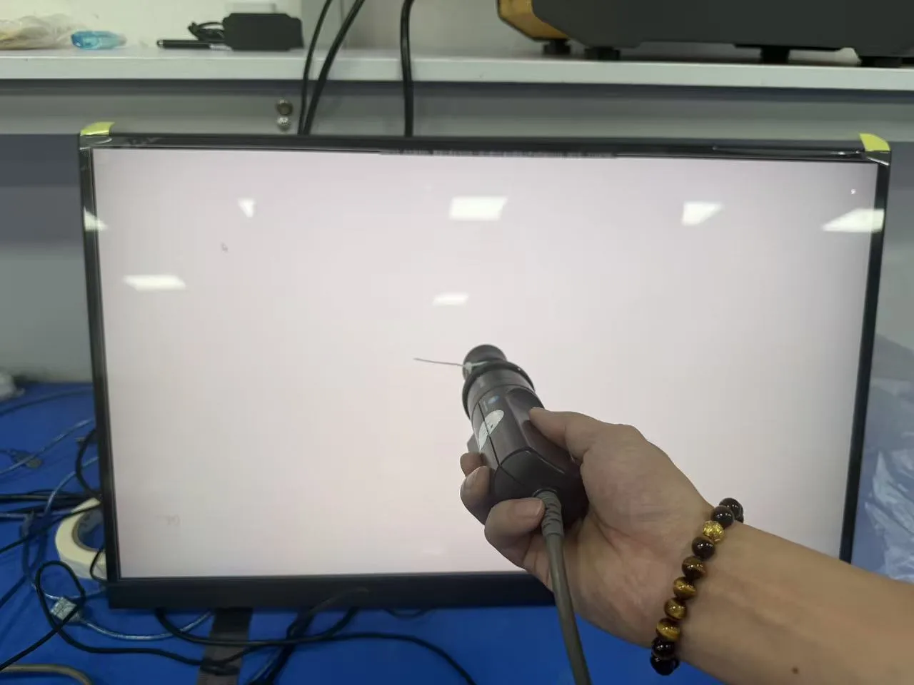 Measuring probe aimed at the center of a monitor showing a full-screen white test image